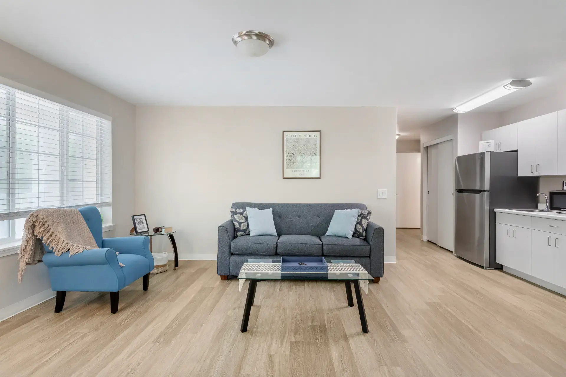 Furnished living room with sofas and kitchen with refrigerator and hardwood floors.