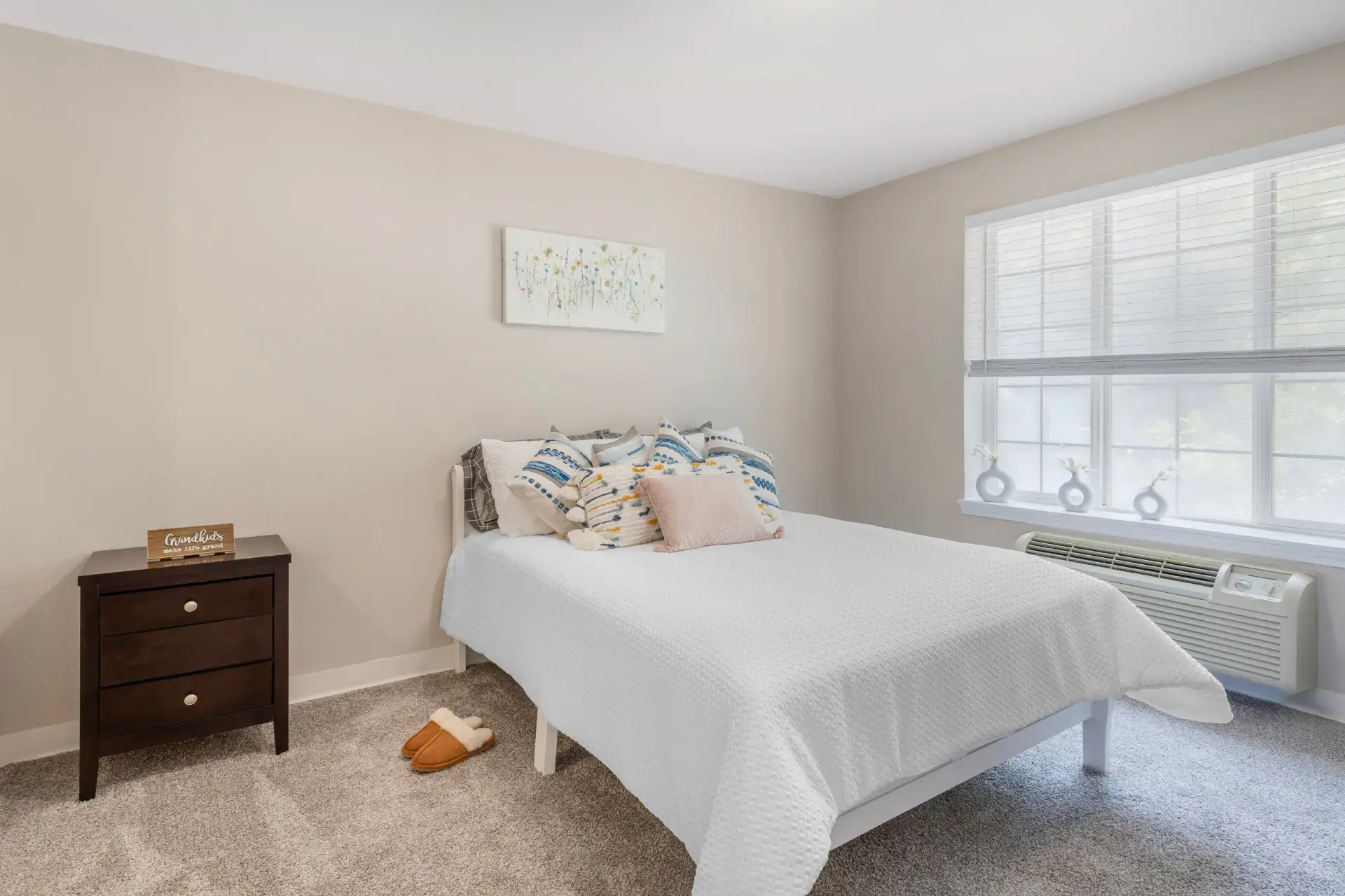 Bedroom with pillows, artwork on wall, side table, and a window with a view.